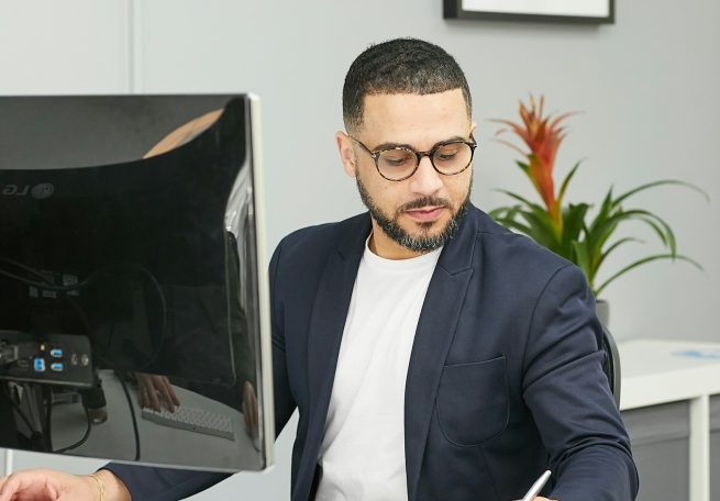 Mann mit Brille, der am Schreibtisch sitzt und Notizen macht. Pflanze im Hintergrund.